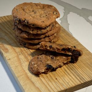 Stack of cinnamon raisin oatmeal cookies on a wooden board with one cookie broken open to show the oats and raisins