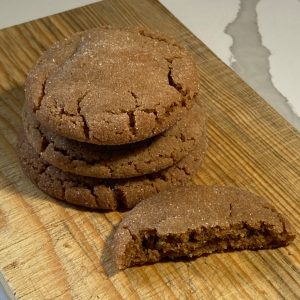 Stack of sugar-rolled cinnamon spice cookies with crackled tops on a wooden board, with half a cookie in front