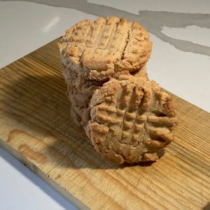 Stack of peanut butter cookies with crisscross fork marks on a wooden board, one cookie leaning against the front