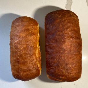 Small and large loaves of white sourdough sandwich bread side by side, seen from above on a white counter